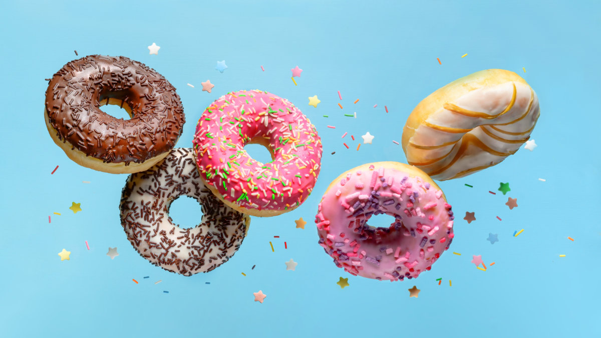 mix of multicolored doughnuts with sprinkel flying on blue background.